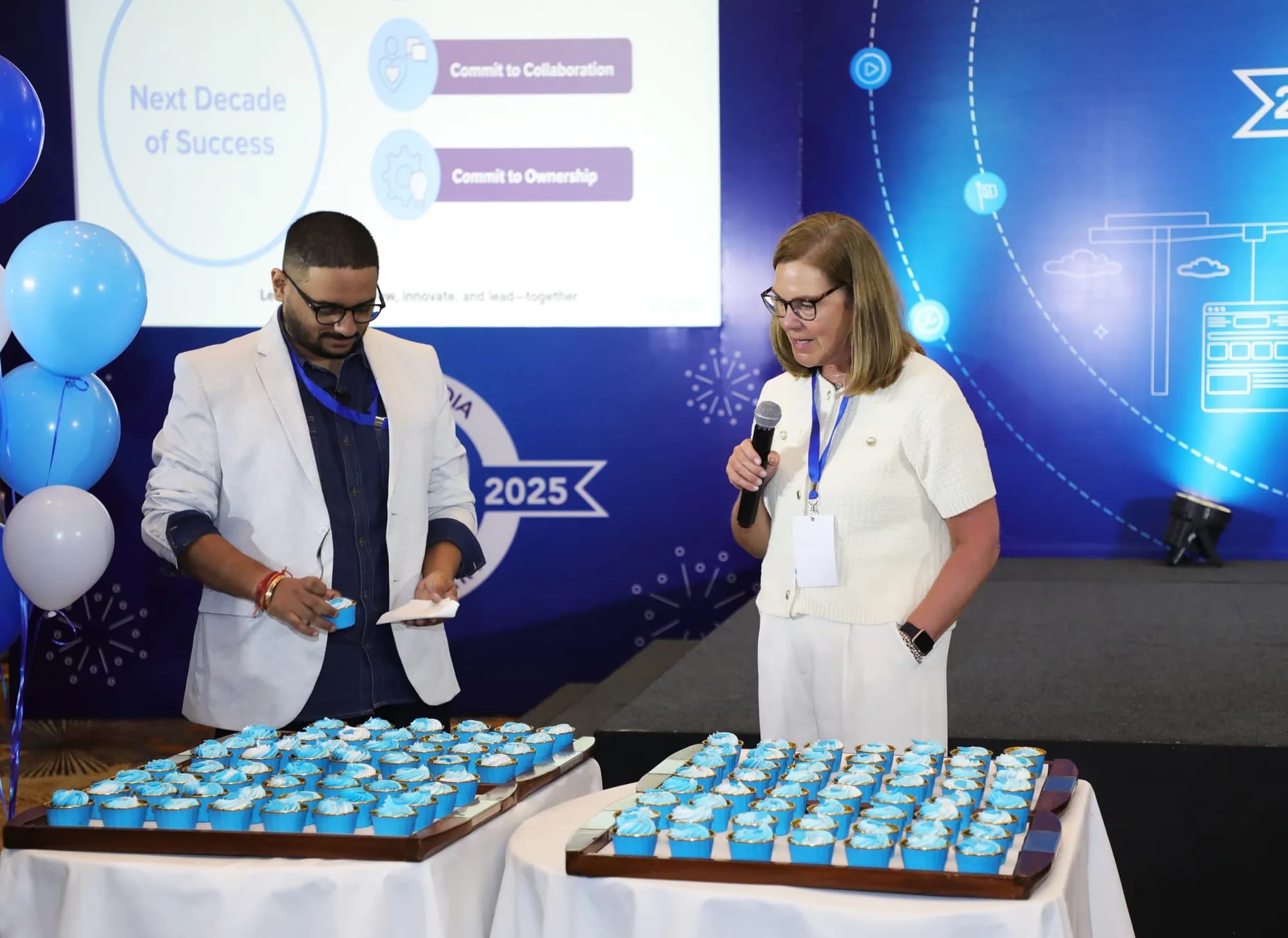 Presenters on stage beside a table of branded cupcakes