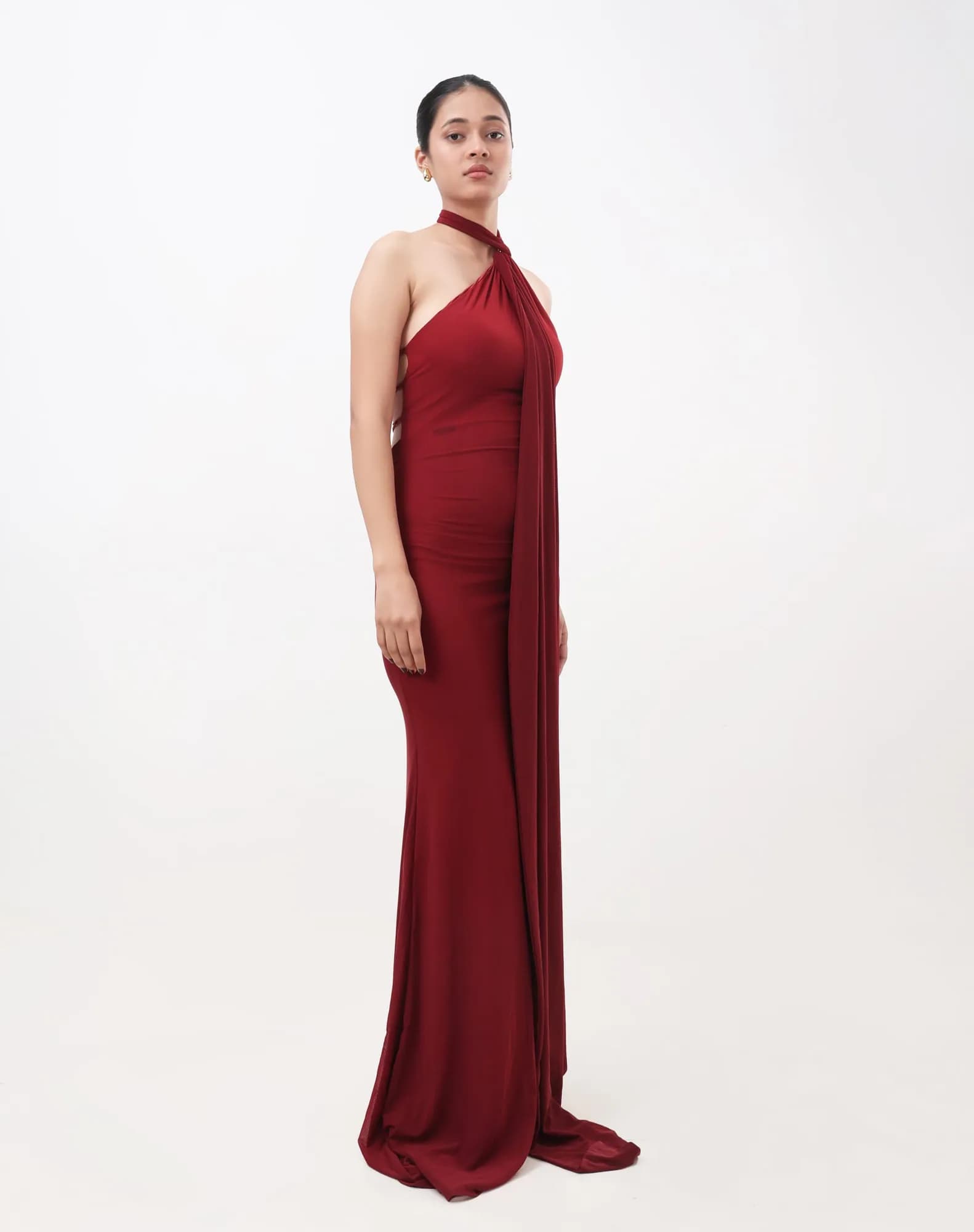 Model in a red halter-neck gown standing against a white studio backdrop