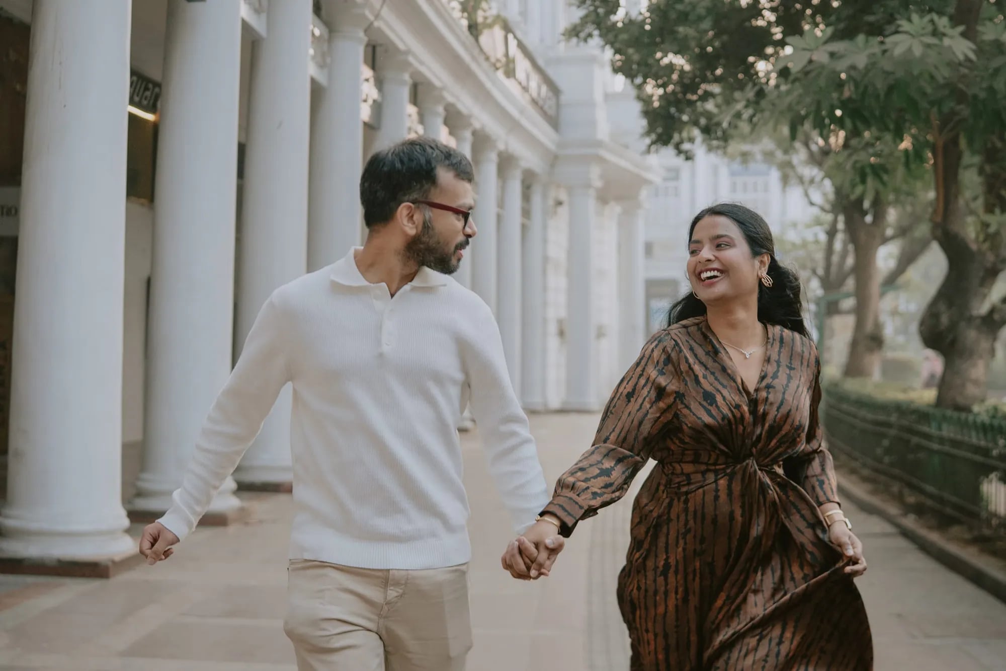 Couple running hand in hand along a white colonnade